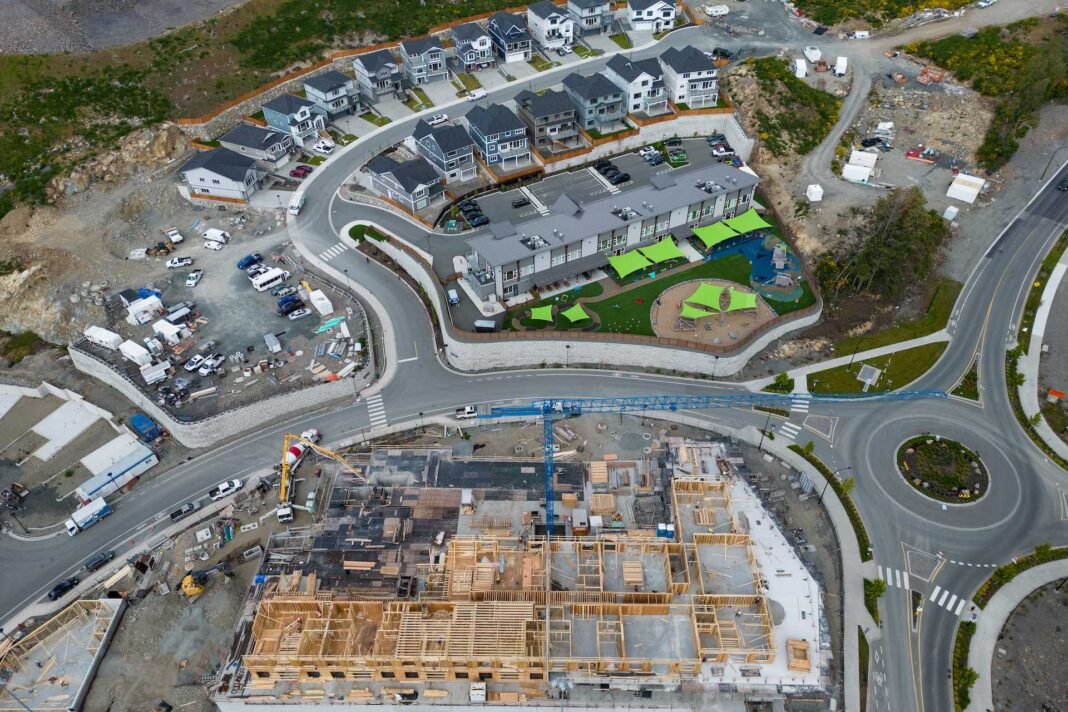 An aerial photo of a partially built housing development, with curving streets and newly finished homes, along with a large complex that is still under construction. A traffic circle is visible on the lower right side of the frame.