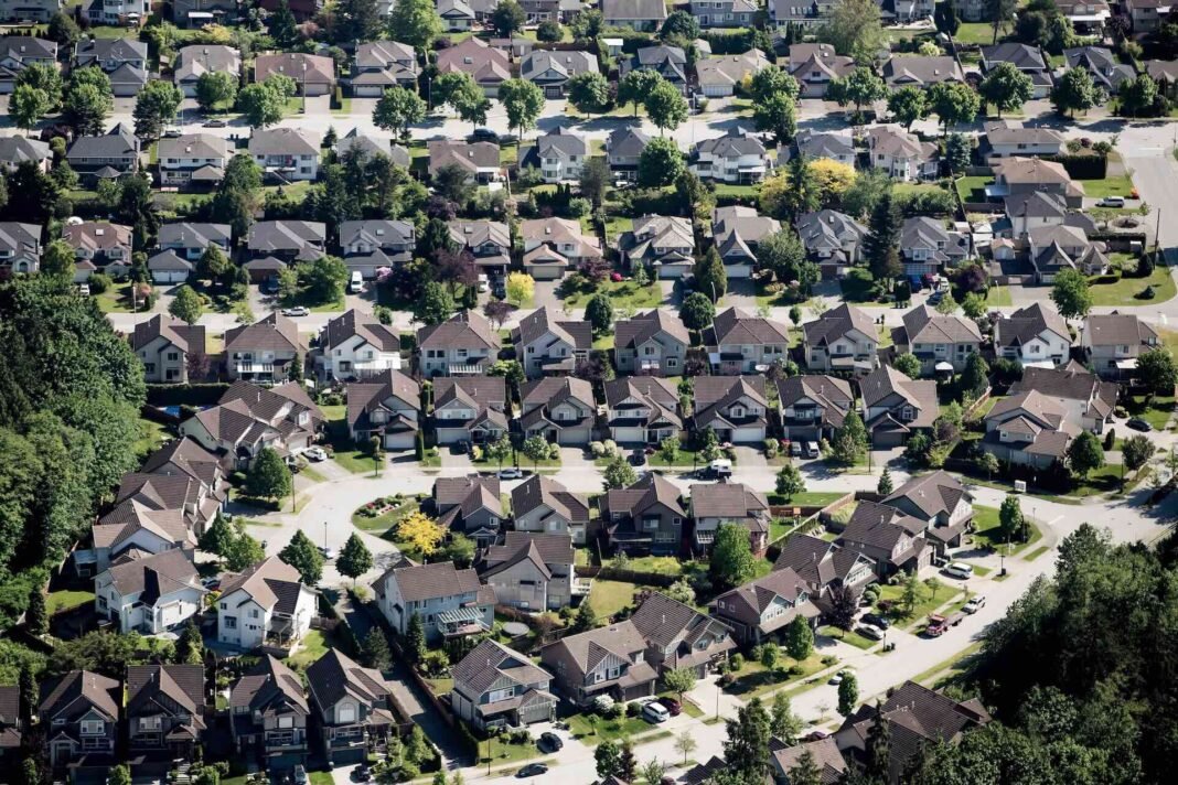 An aerial view of suburban housing dotted with green trees.